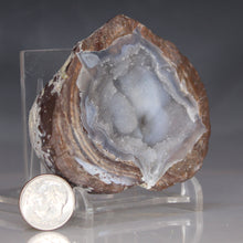 Load image into Gallery viewer, Geode with internal crystal structure on a clear stand, next to a coin for scale, against a dark background