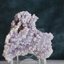 Load image into Gallery viewer, A cluster of druzy soft purple grape agate stones displayed on a clear acrylic stand against a dark background.