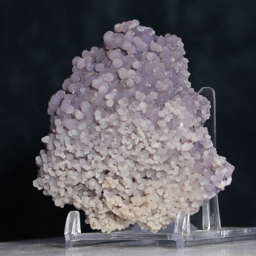 A cluster of soft lavender grape agate micro spheres displayed on a clear acrylic stand against a black background.