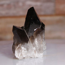 Load image into Gallery viewer, Smoky crystal on a reflective surface with a blurred background
