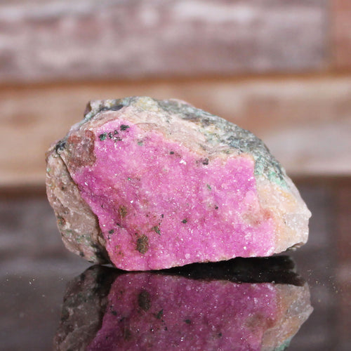 Raw pink crystal on a reflective surface with a blurred background