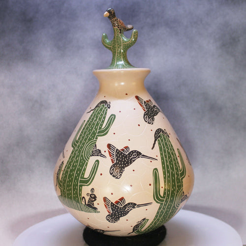 Ceramic Mata Ortiz vase with cactus and hummingbird designs on a gray background